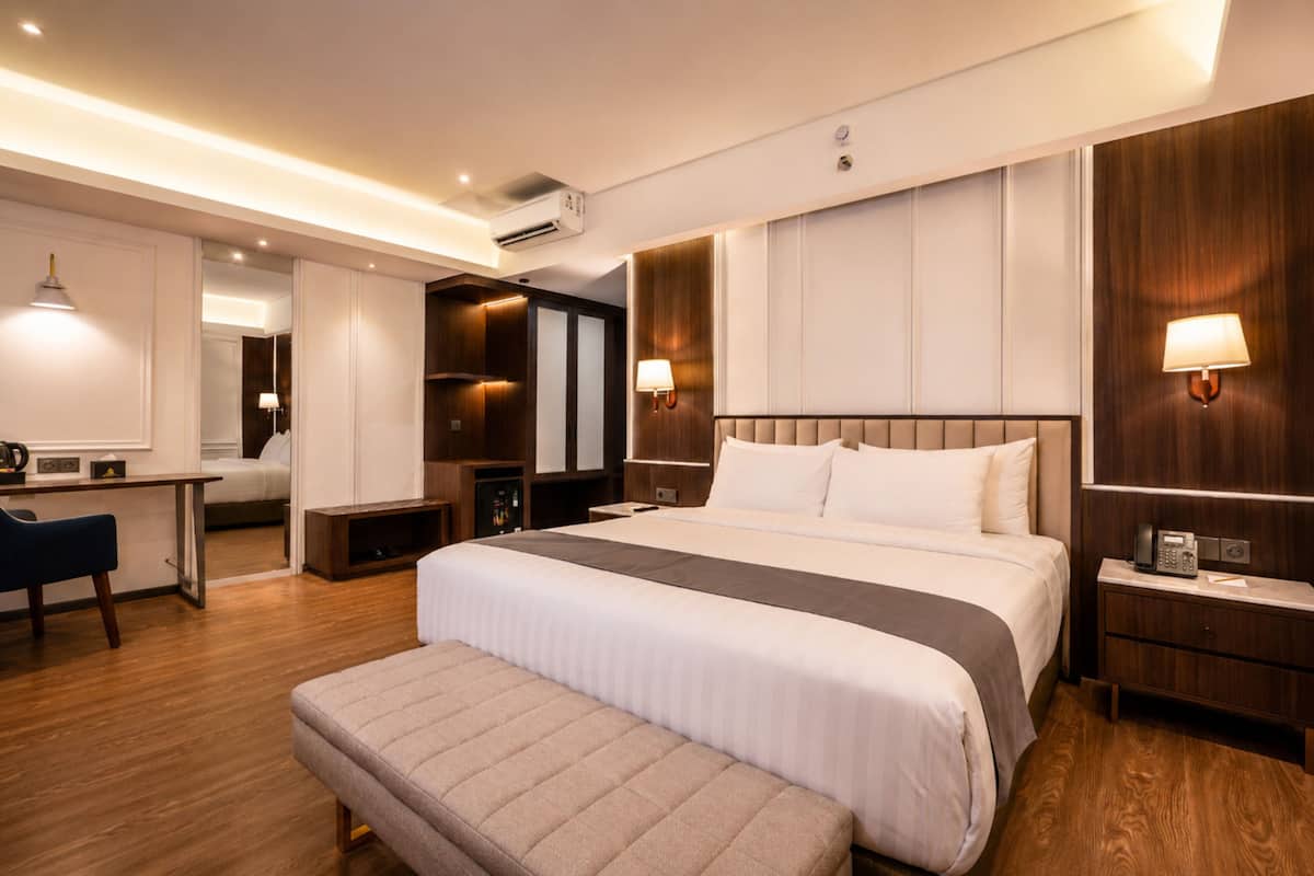 Quarto de hotel moderno com uma cama grande, mesas de cabeceira, uma escrivaninha e um espaço de estar.