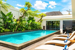 Una piscina al aire libre, sombrillas, sillones reclinables de piscina