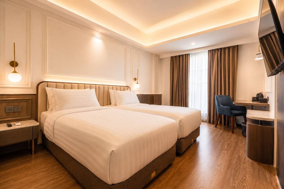 Quarto de hotel com duas camas, uma escrivaninha, uma cadeira e uma televisão.