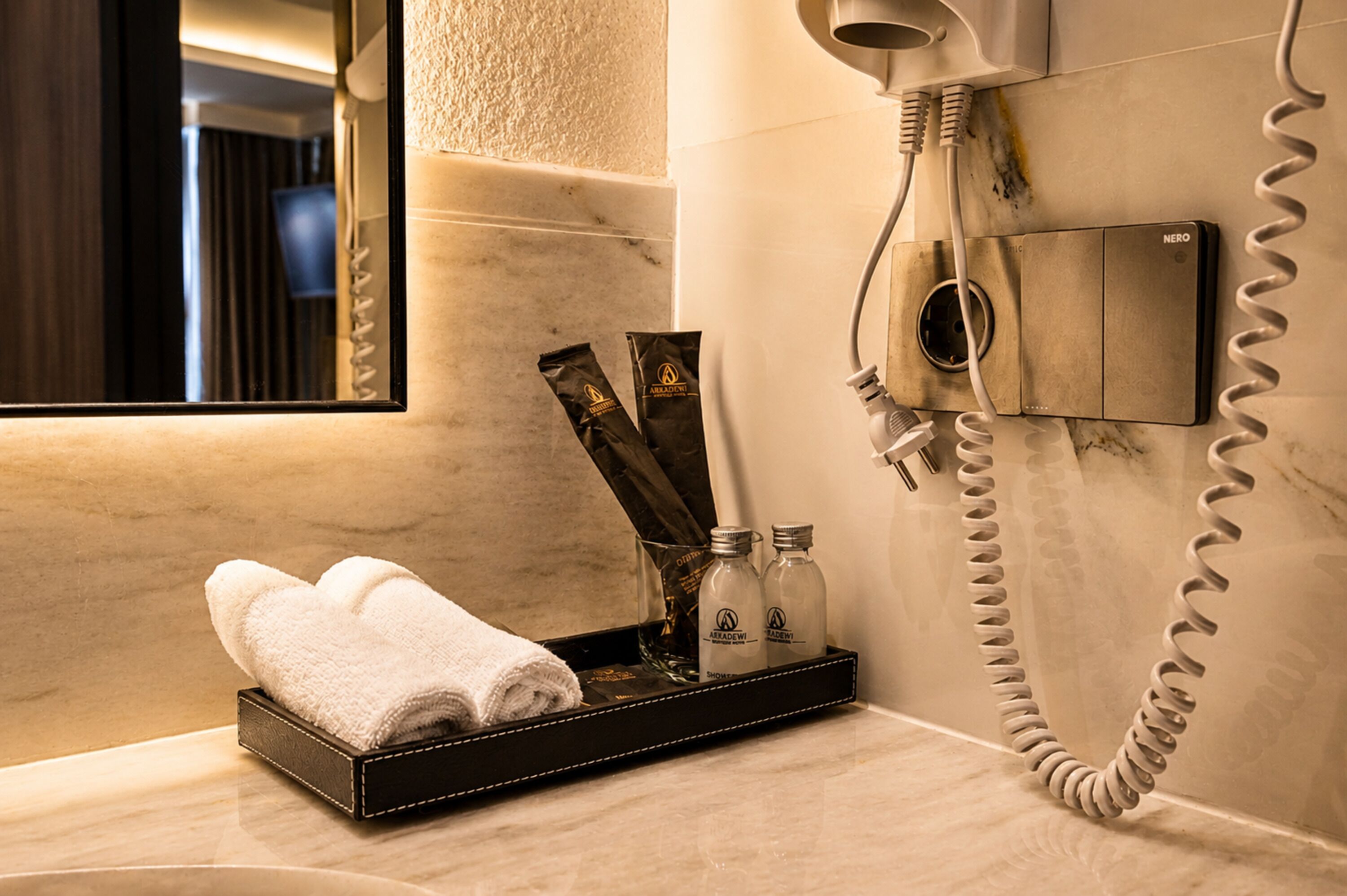Ein Badezimmer mit Fön, Spiegel, Tablett mit Handtüchern und Pflegeprodukten sowie einem an der Wand montierten Telefon.