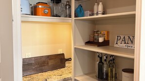 Un garde-manger bien organisé, avec des étagères contenant des appareils de cuisine, des boîtes de rangement et une pancarte indiquant « USTENSILES DE CUISINE ».