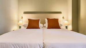 Ein Doppelbett mit weißen Laken und zwei braunen Kissen, das von zwei Nachttischlampen gesäumt wird.