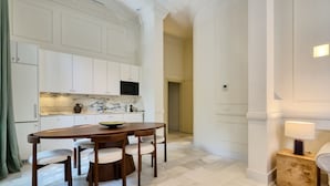 Uma cozinha moderna com armários brancos, bancada de mármore e uma área de refeições com mesa e cadeiras de madeira.