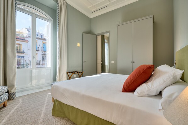 A hotel room with a large bed, a view of buildings through a glass door, and a wardrobe.