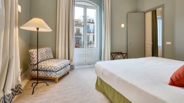 Quarto de hotel com cama, uma cadeira, abajur e vista da cidade pela janela.