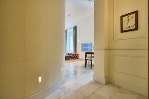 A hotel corridor with a flat-screen TV on a stand, a colorful ottoman, and a framed artwork on the wall.