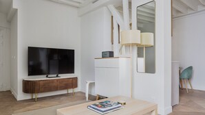 Uma sala de estar moderna com uma televisão de tela plana, um console de madeira, um armário branco, um banquinho branco pequeno, uma mesa de centro de madeira e uma poltrona azul-turquesa.