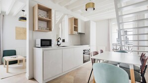 Uma cozinha moderna com armários brancos, micro-ondas embutido e área de jantar com mesa e cadeiras brancas.