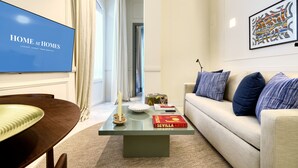 A modern living room with a flat-screen TV, a coffee table with a book and decorative items, a beige sofa with patterned cushions, and a framed abstract painting on the wall. - Adriano 1.4 by Home at Homes (Sevilla)