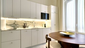A modern kitchen with white cabinets, a marble countertop, a microwave, and a dining area with a round table and chairs. - Adriano 1.4 by Home at Homes (Sevilla)