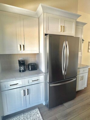 Eine moderne Küche mit weißen Schränken, einem Edelstahl-Kühlschrank und einer Kaffeemaschine auf der Arbeitsfläche.