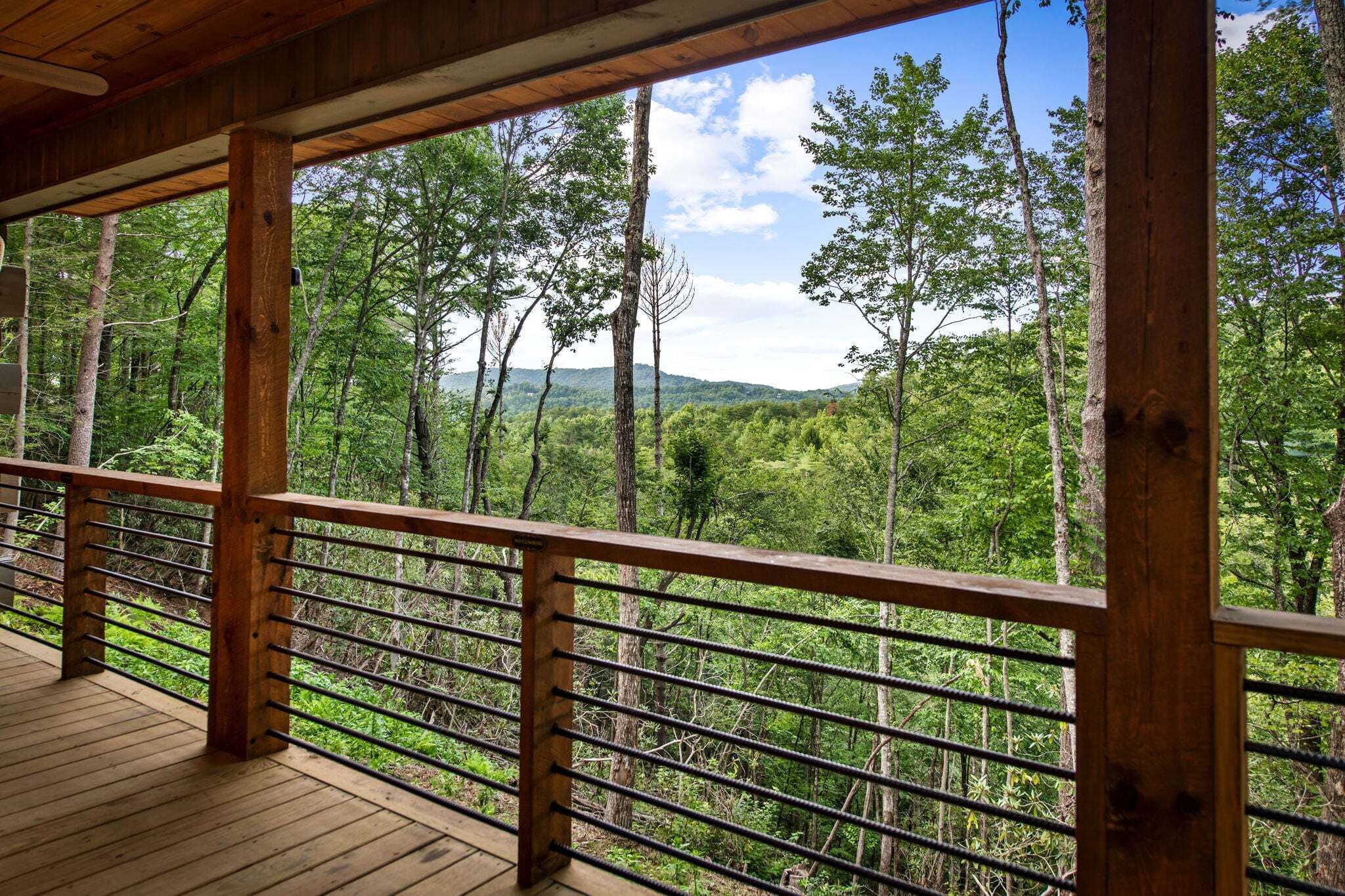 A wooden deck with a metal railing overlooking a forested area.