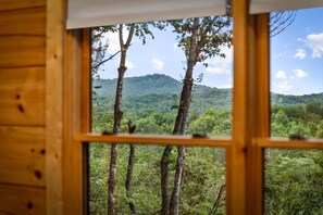 Uma janela com vista para uma paisagem montanhosa arborizada.
