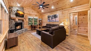 Ein Ferienhäuschen mit Kamin aus Stein, Holzwänden, Deckenventilator und einer Couch.
