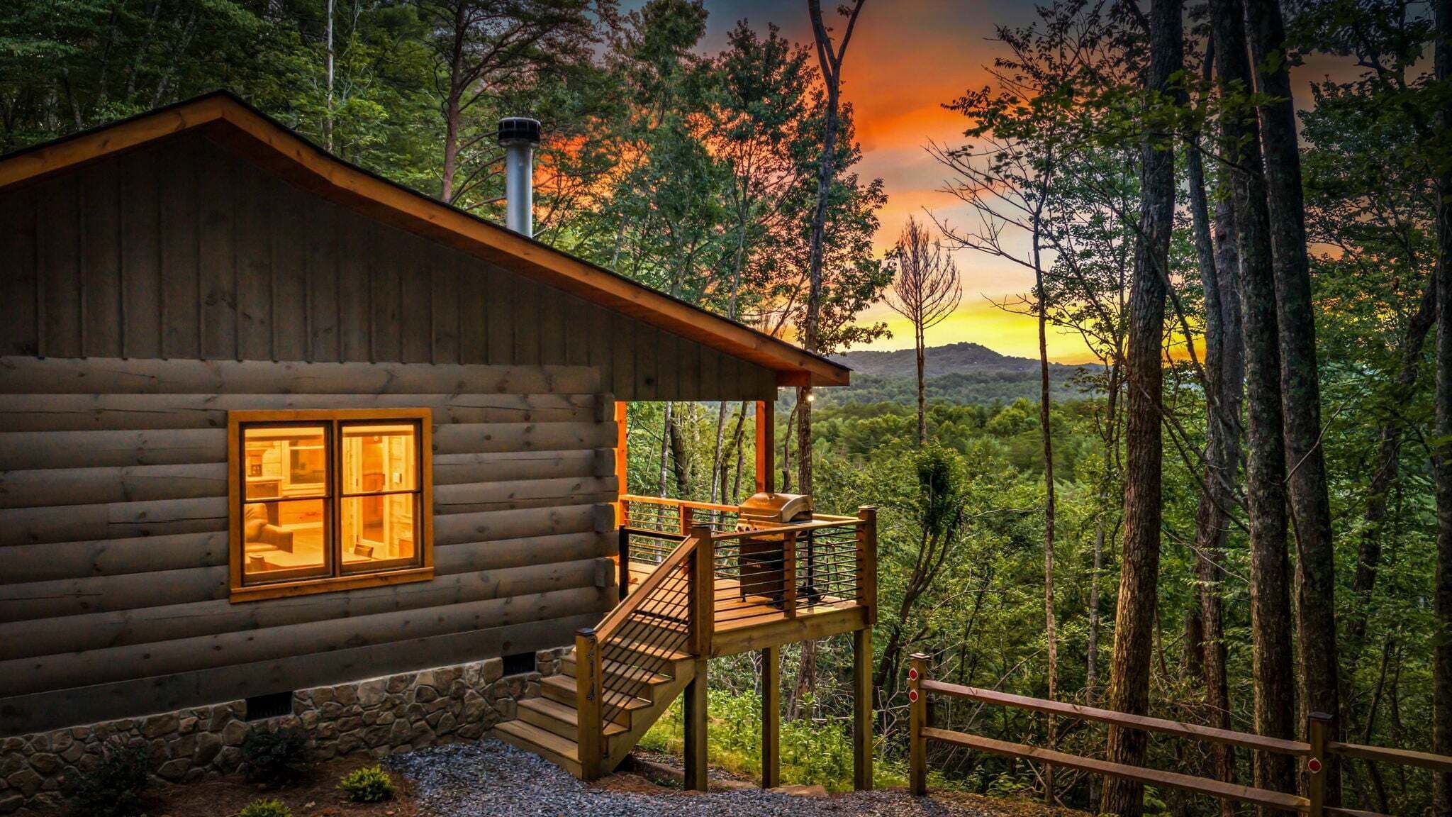 A log cabin with a balcony, a chimney, and a view of a forested landscape.