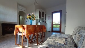 A room with a bed, a dining table with chairs, a vase with flowers, a fireplace, and a view through a door to a balcony. - Wonderful view of the island of Tavolara (Monte Petrosu)