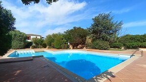 A rectangular swimming pool with a tiled deck, surrounded by lush greenery and trees. - Wonderful view of the island of Tavolara (Monte Petrosu)
