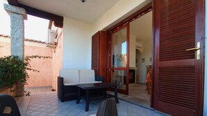 A patio with a sofa, a table, and a chair. There is a wooden door and a tiled floor. - Wonderful view of the island of Tavolara (Monte Petrosu)