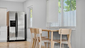 A kitchen with a stainless steel refrigerator, wooden chairs, a table, and windows with blinds. - Harbor Haven in Fort Lauderdale (Fort Lauderdale)