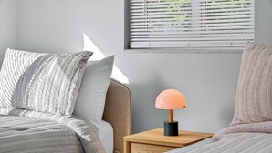 A neatly made bed with striped bedding, a bedside table with a lamp, and a window with blinds. - Harbor Haven in Fort Lauderdale (Fort Lauderdale)