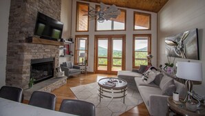 A spacious living room with a fireplace, large windows, and a ceiling fan.