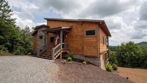 A modern wooden house with a stone entrance, a porch, and a flag.