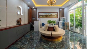 A hotel lobby with a reception desk, a seating area with a round table, a chandelier, and a large window with a view of greenery. - Anna Hotel Phu Quoc - Sunset Town Tour - Infinity Pool Access (Phu Quoc)