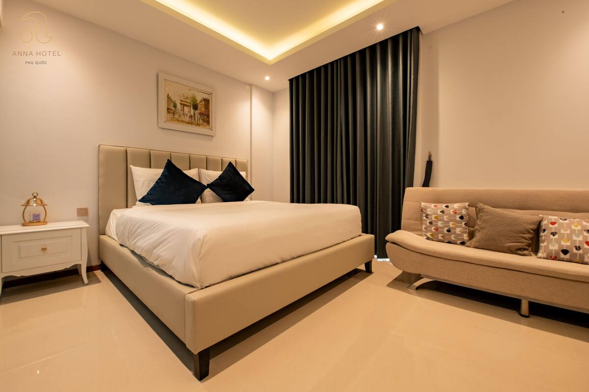 A modern bedroom with a bed, a sofa, a nightstand, and a wall-mounted picture.