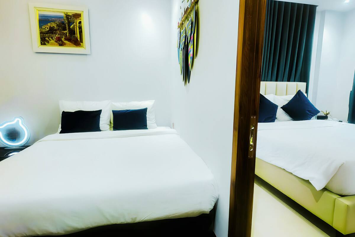 A hotel room with a bed, bedside table, and a neon sign.