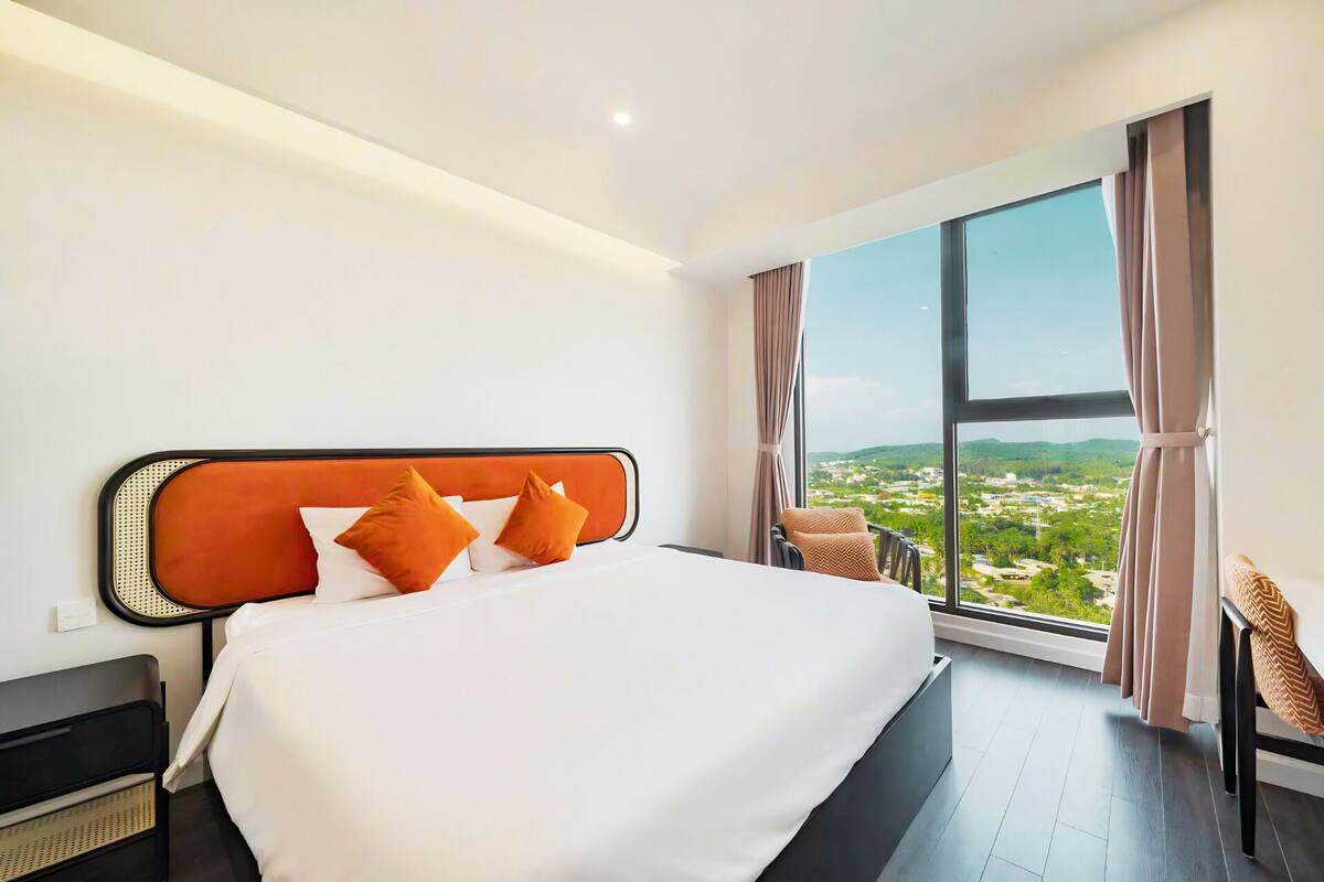 A hotel room with a large bed, a view of a cityscape, and a window with curtains.