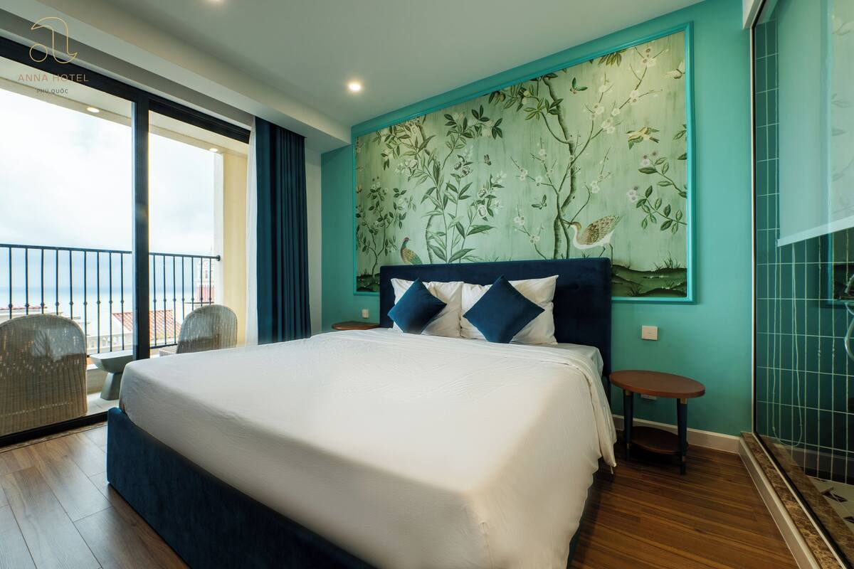 A hotel room with a large bed, a balcony with wicker chairs, and a mural on the wall.
