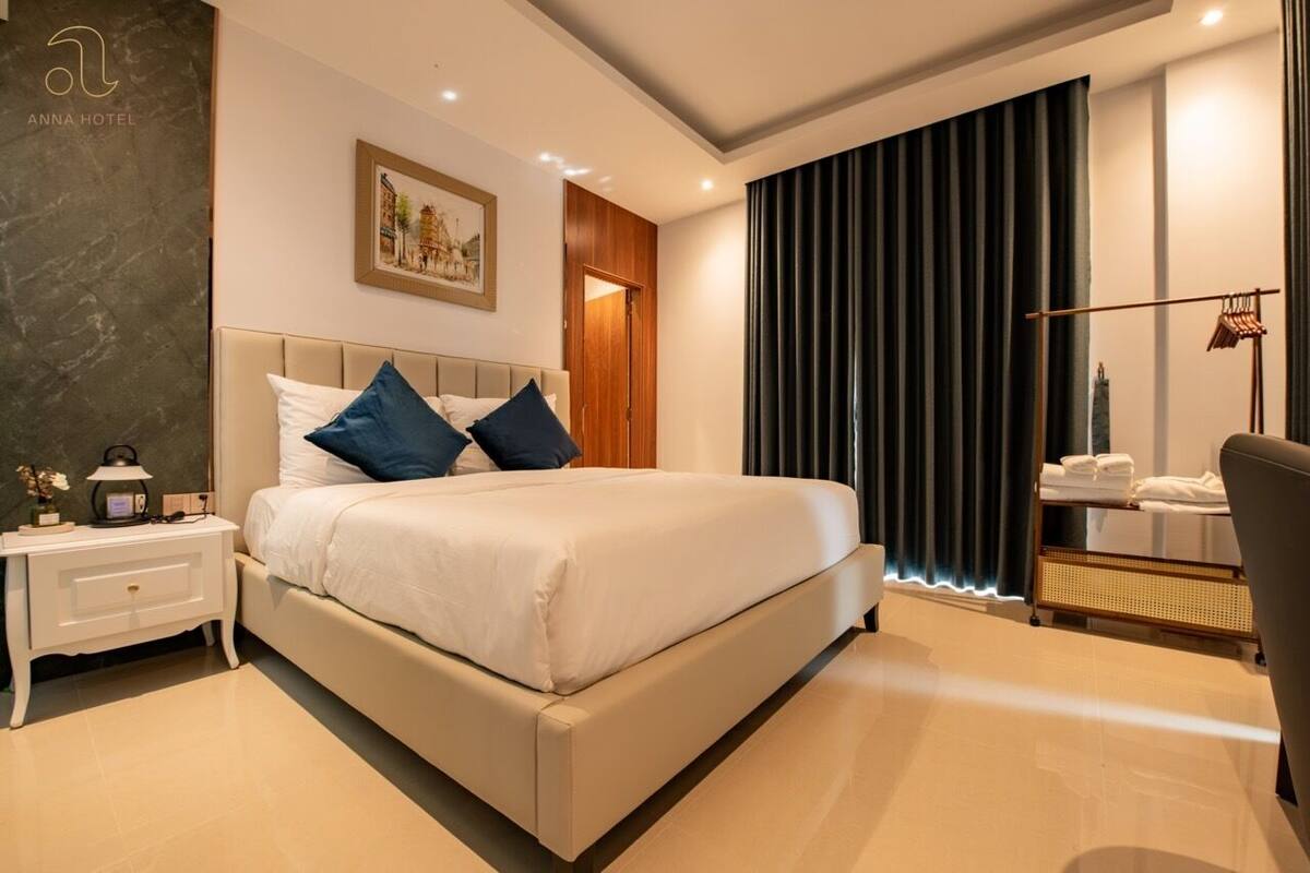 A modern hotel room with a large bed, a nightstand, a lamp, a framed picture on the wall, and a window with curtains.