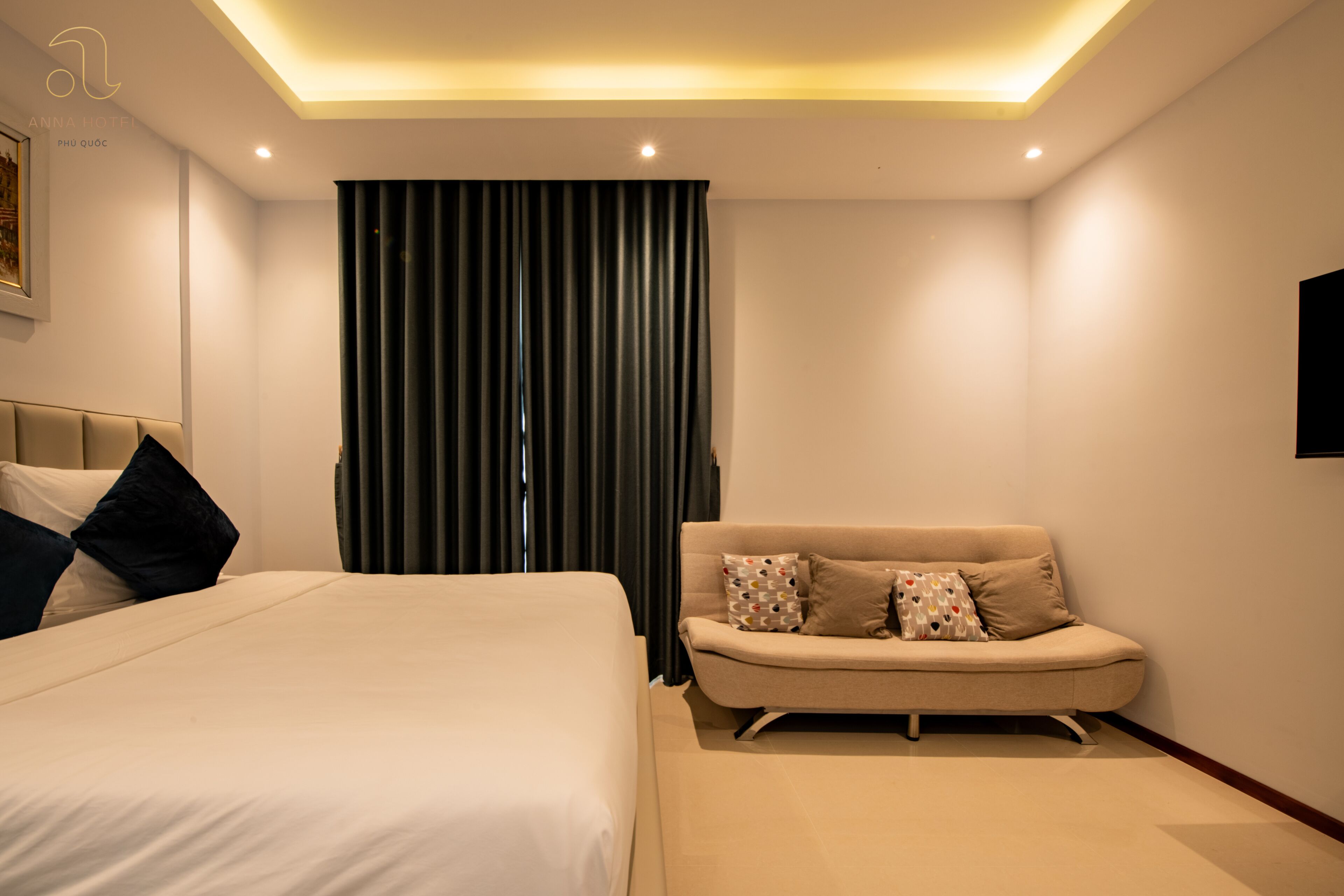 A modern hotel room with a large bed, a sofa, and a television mounted on the wall.