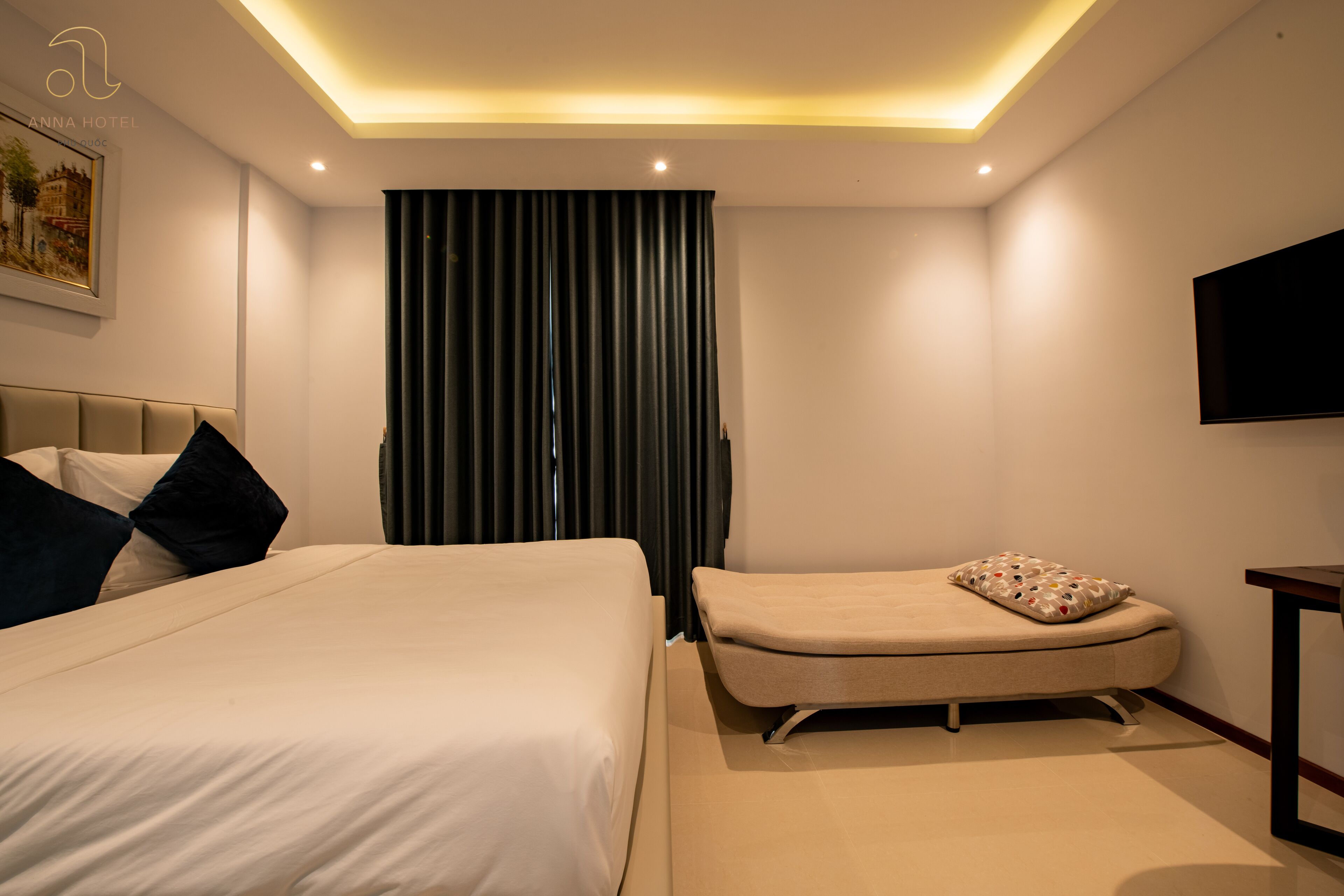 Une chambre d’hôtel moderne dotée d’un grand lit, d’un petit canapé, d’un téléviseur à écran plat fixé au mur et d’un luminaire au plafond.