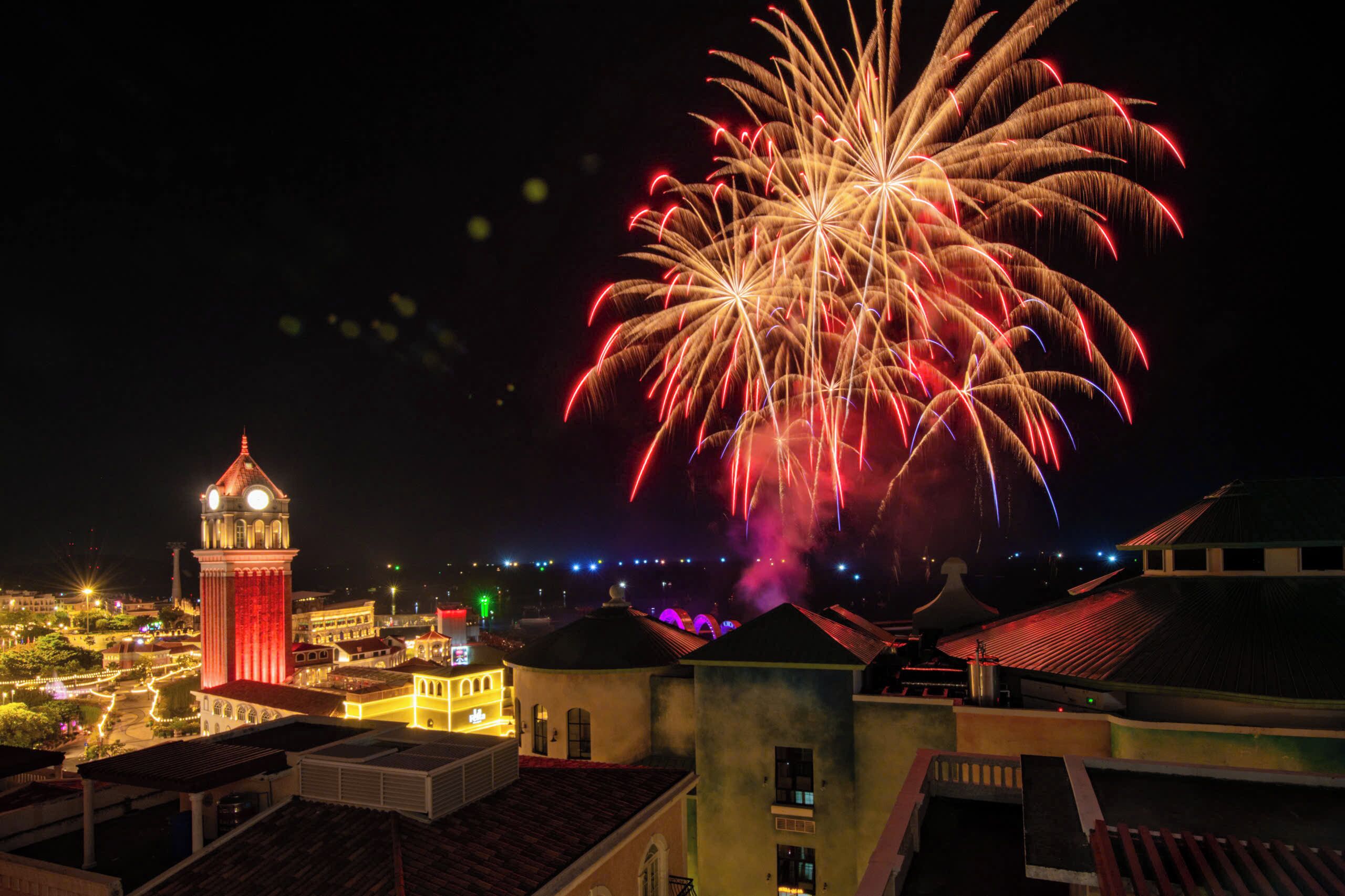A night view of a cityscape with a prominent clock tower and fireworks in the sky.