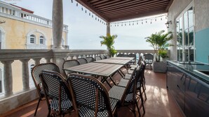 A covered outdoor dining area with a long table and multiple chairs, a bar counter, and a view of a building with columns and arched windows. - Anna Hotel Phu Quoc - Sunset Town Tour - Infinity Pool Access (Phu Quoc)