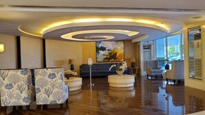 A hotel lobby with a modern design, featuring a central seating area with a sofa and ottomans, a large abstract painting on the wall, and a large window providing a view outside. - Dainty Pasay City Apartment for Rent - Entire House Front of Mall of Asia (Pasay)
