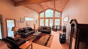 Un salón amplio con dos sofás de cuero, una mesa de centro y una chimenea. Ventanas grandes ofrecen luz natural y vistas al exterior.
