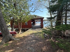 A red wooden cabin with a dock extending into a lake, surrounded by trees. - New Listing! Peaceful Oceanfront Home with Dock, Decks, and Shore Access in Cundy’s Harbor (Harpswell)