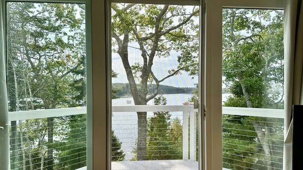 Uitzicht vanaf een balkon, met een grote boom en een waterpartij op de achtergrond.