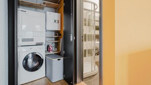 Une petite buanderie équipée d’un lave-linge, d’un sèche-linge et d’une planche à repasser.