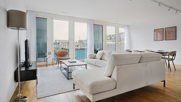 Un salon moderne avec un canapé, une table basse et un téléviseur posé sur un meuble. Il y a un balcon avec vue sur la ville.