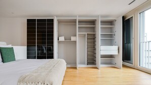 Une chambre avec un grand lit, une armoire à plusieurs compartiments et une porte-fenêtre coulissante sur le côté droit.