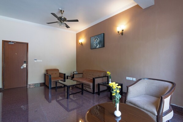 Un hall d’entrée avec un ventilateur de plafond, un canapé, deux fauteuils, une table basse et un vase rempli de fleurs.
