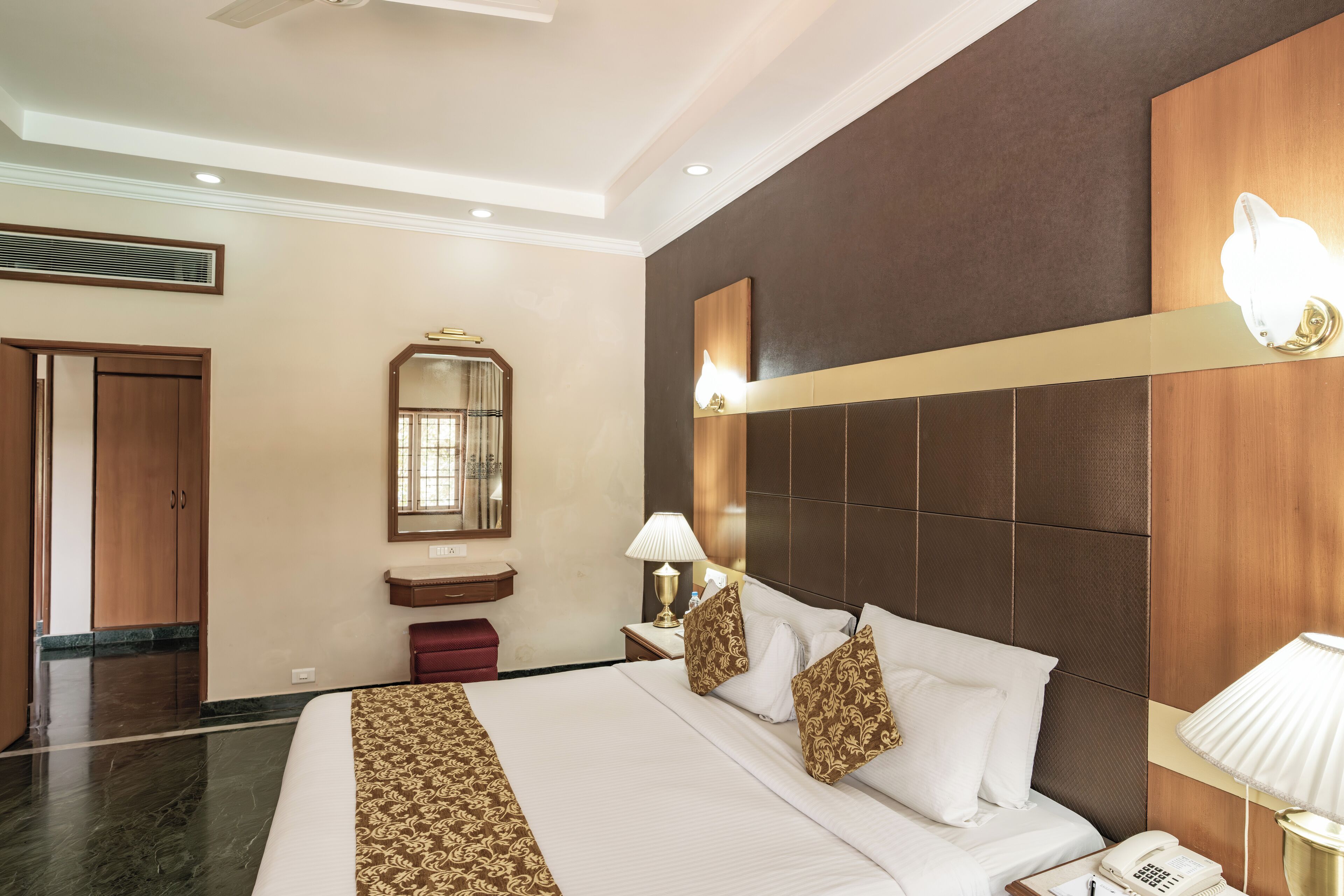 A hotel room with a large bed, a bedside table with a lamp, a mirror, and a wooden headboard.