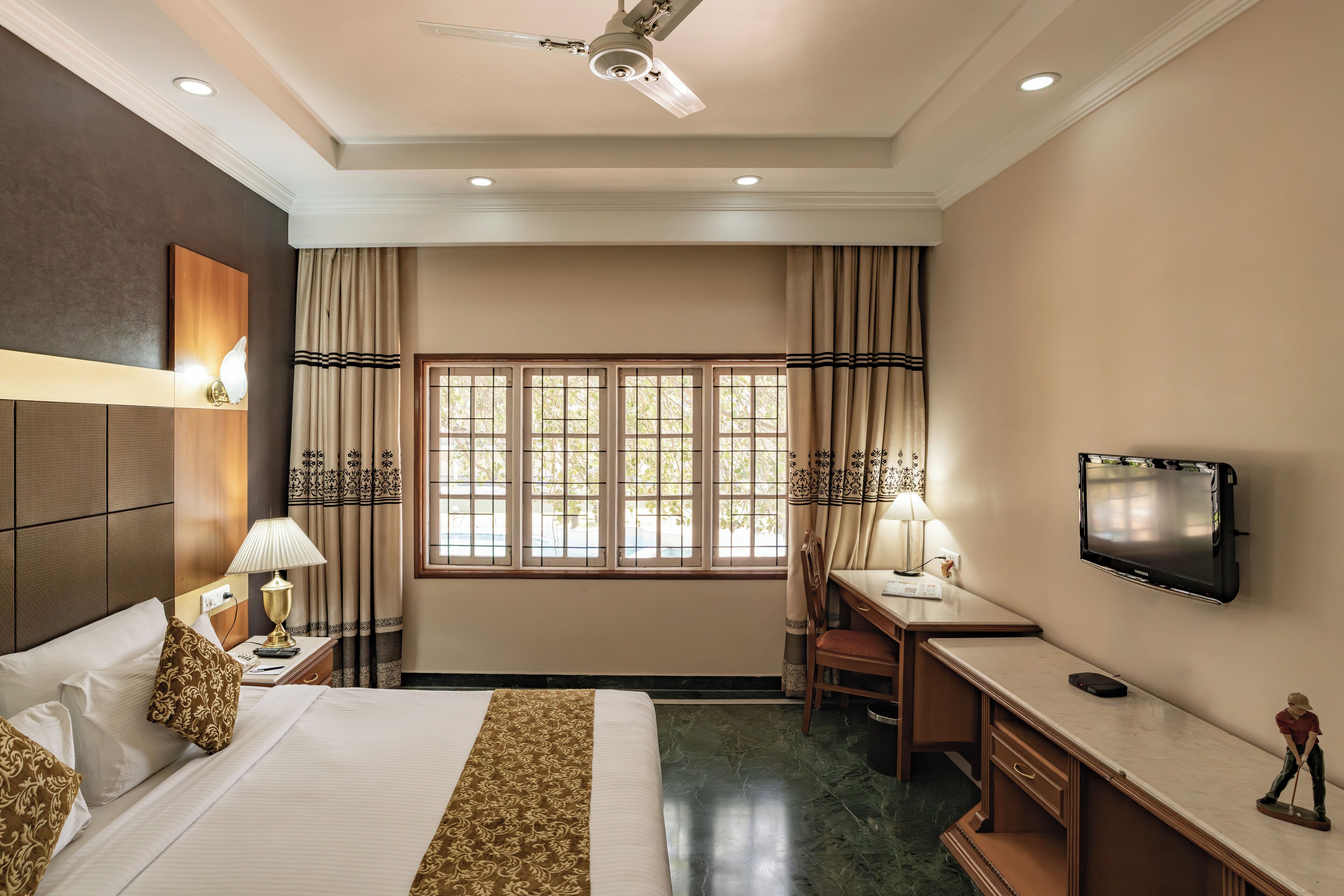 A hotel room with a bed, desk, chair, TV, and window with curtains.