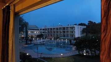 Habitación de hotel con un amplio ventanal que da a un patio con piscina y un edificio al fondo.