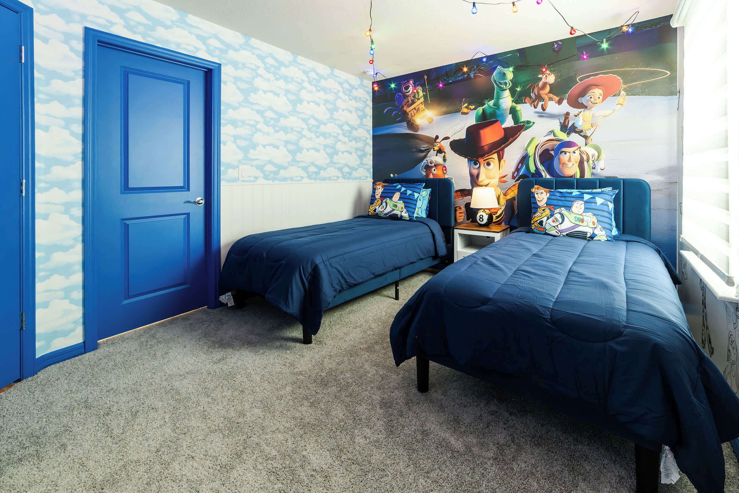 A bedroom with two single beds, a mural on the wall, and a door with a cloud pattern.