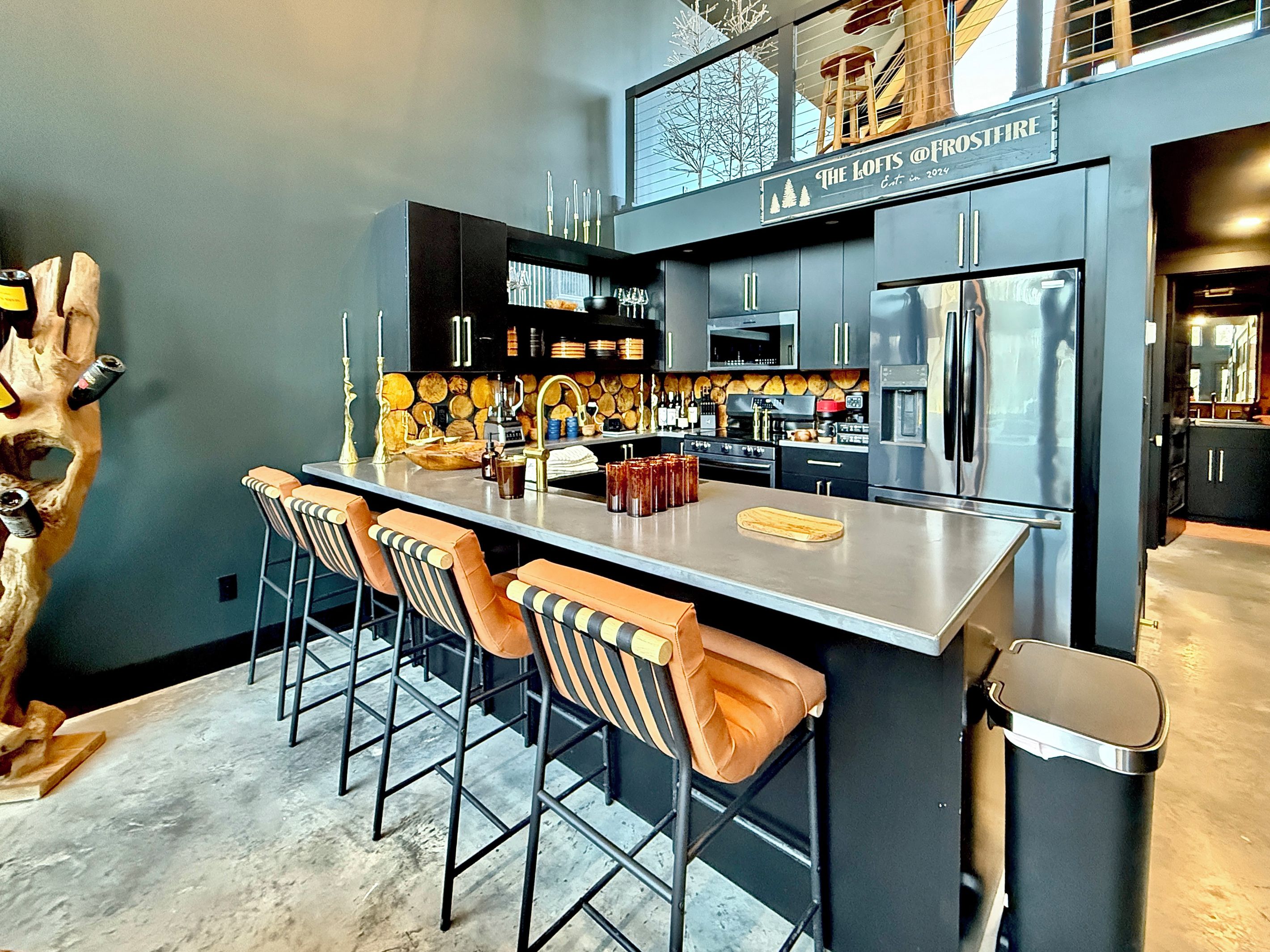 A modern kitchen with a bar area, stainless steel appliances, and a unique wooden sculpture.