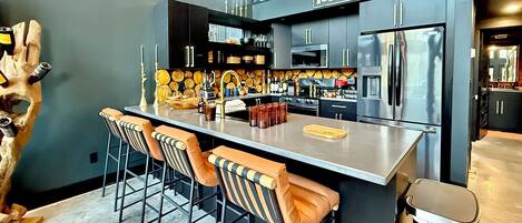 A modern kitchen with a bar area, stainless steel appliances, and a unique wooden sculpture.